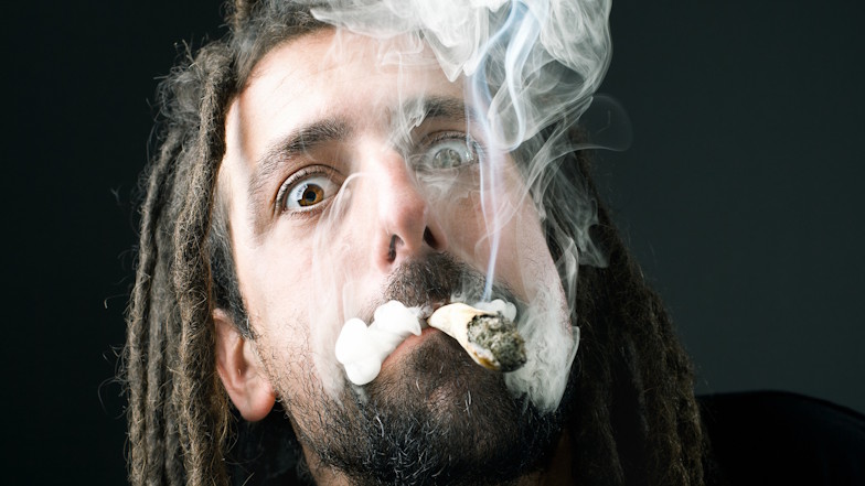 Mann mit qualmendem Joint im Mund vor schwarzem Hintergrund